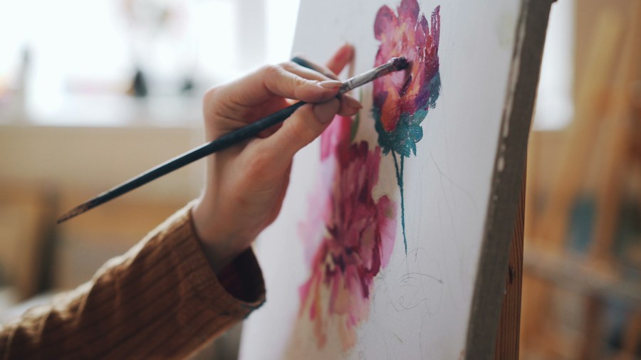 Une main peint une fleur sur une toile avec un pinceau
